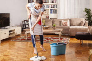 A professional maid in a tan apron using a map and bucket to clean the floors of a living room in St. Charles and St. Louis, MO.
