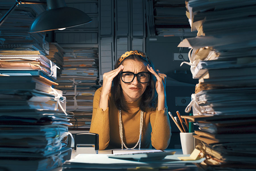 A woman sitting at her desk with a messy and cluttered office in St. Charles, MO, and needing professional maid cleaning services.