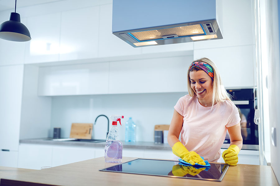 A professional maid in a light pink t-shirt with yellow gloves smiling while cleaning the kitchen of a home in St. Charles, MO.