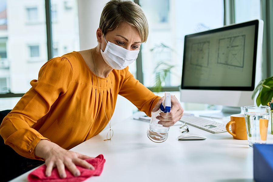 A woman in a yellow shirt sprays and wipes down her desk with a cleaning solution to deep clean her office space in St Louis, MO.