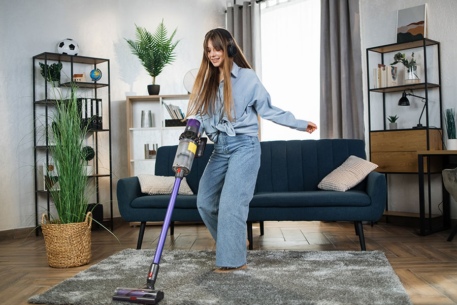 A young woman in St. Louis, MO, vacuuming the grey area rug in her living room.